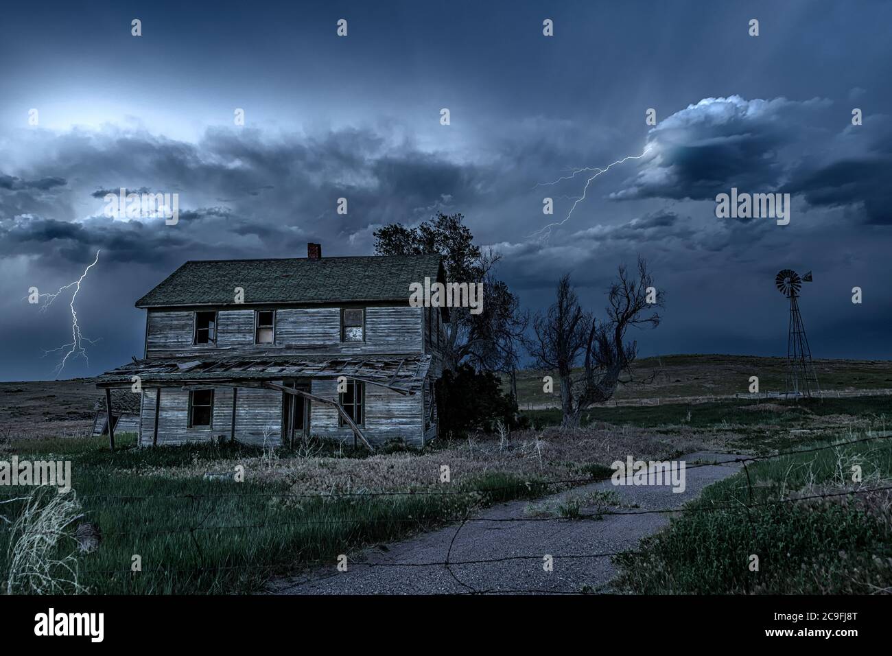 Eine lange Exposition eines alten, verfallenen Spukhauses im ländlichen Mittleren Westen bei Nacht, eingerahmt von unheimlichem dunklen Himmel und Blitz. Stockfoto
