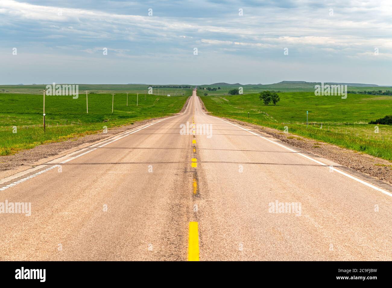 Abnehmende Perspektive einer ländlichen Straße in der Great Plains, umgeben von grünen Ackerland und riesigen Ländern. Stockfoto