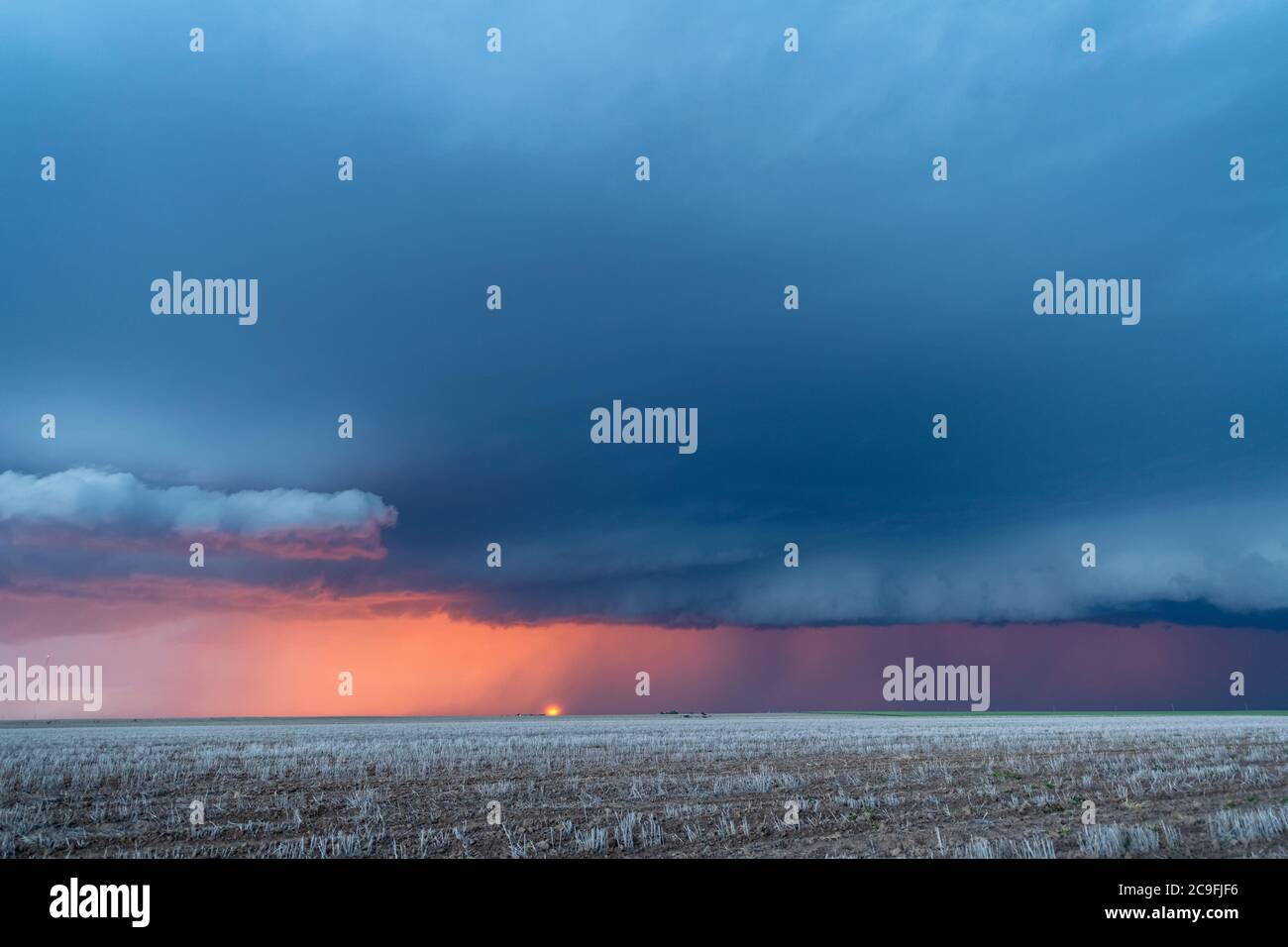 Ein großer Sturm zieht sich durch die Great Plains, während die Sonne hinter ihr untergeht, während Regen und Blitz den Horizont säumen. Stockfoto