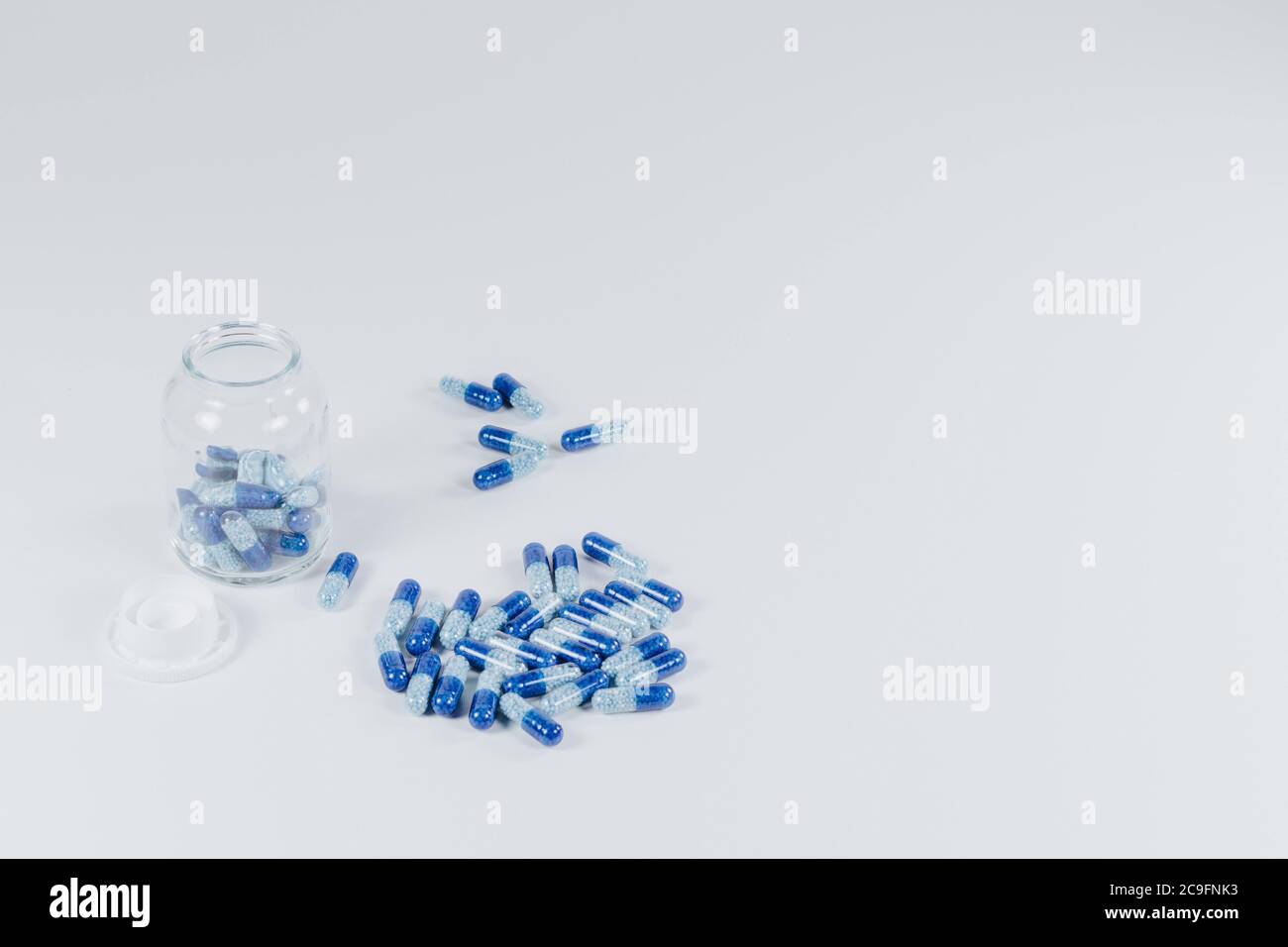 Ein isolierter Nahaufnahme von blauen Pillen im Inneren und neben einem Glasbehälter auf einer weißen Oberfläche Stockfoto