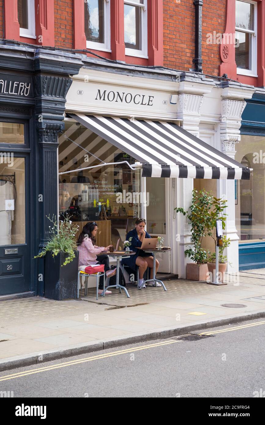 Zwei junge Frauen saßen vor dem Monocle Cafe an Tischen, wo sie sich erfrischen und Laptops benutzten. Chiltern Street, Marylebone, London Stockfoto
