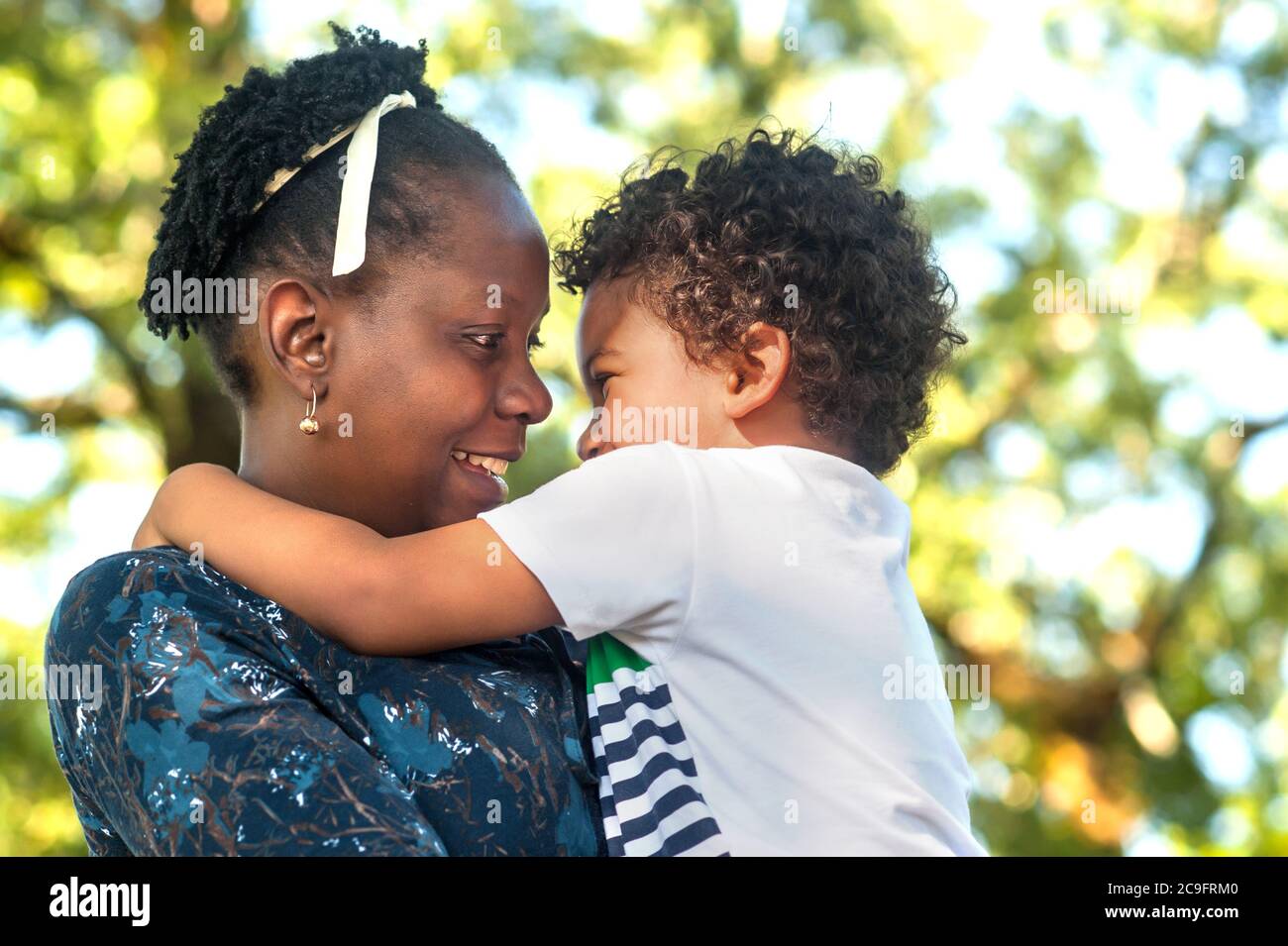 Profilansicht einer glücklichen afrikanischen Mutter, die ihr kleines Kind in der Natur umarmt Stockfoto