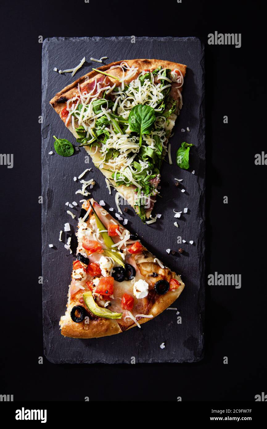 Scheiben heiße Pizza mit Prosciutto, Rucola-Salat, Gemüse, Tomaten und Käse auf Tafel Hintergrund. Draufsicht. Stockfoto