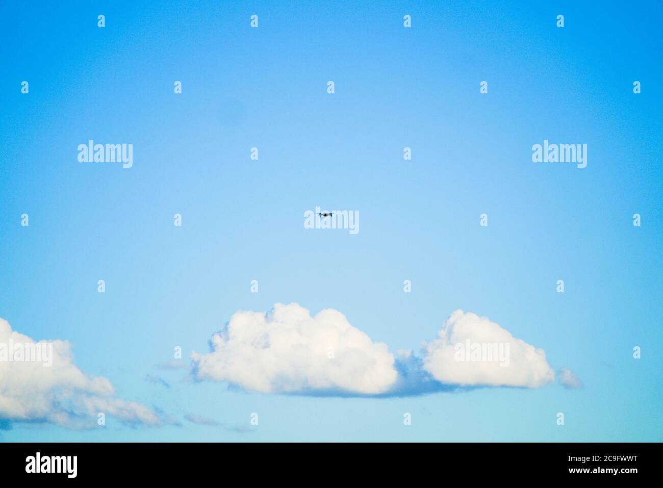 Einzelne Drohne UAV in der Mitte des Bildes mit blauem Himmel und Wolken als Hintergrund, sonniger Tag, vom Boden aufgenommen Stockfoto