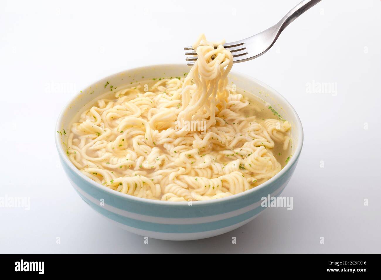 Natriumreich Lebensmittel, schnelle Snacks und Mahlzeiten in Minuten Konzept mit Metallgabel hält Instant Nudeln in einer Keramikschale isoliert auf weißem Hintergrund Stockfoto