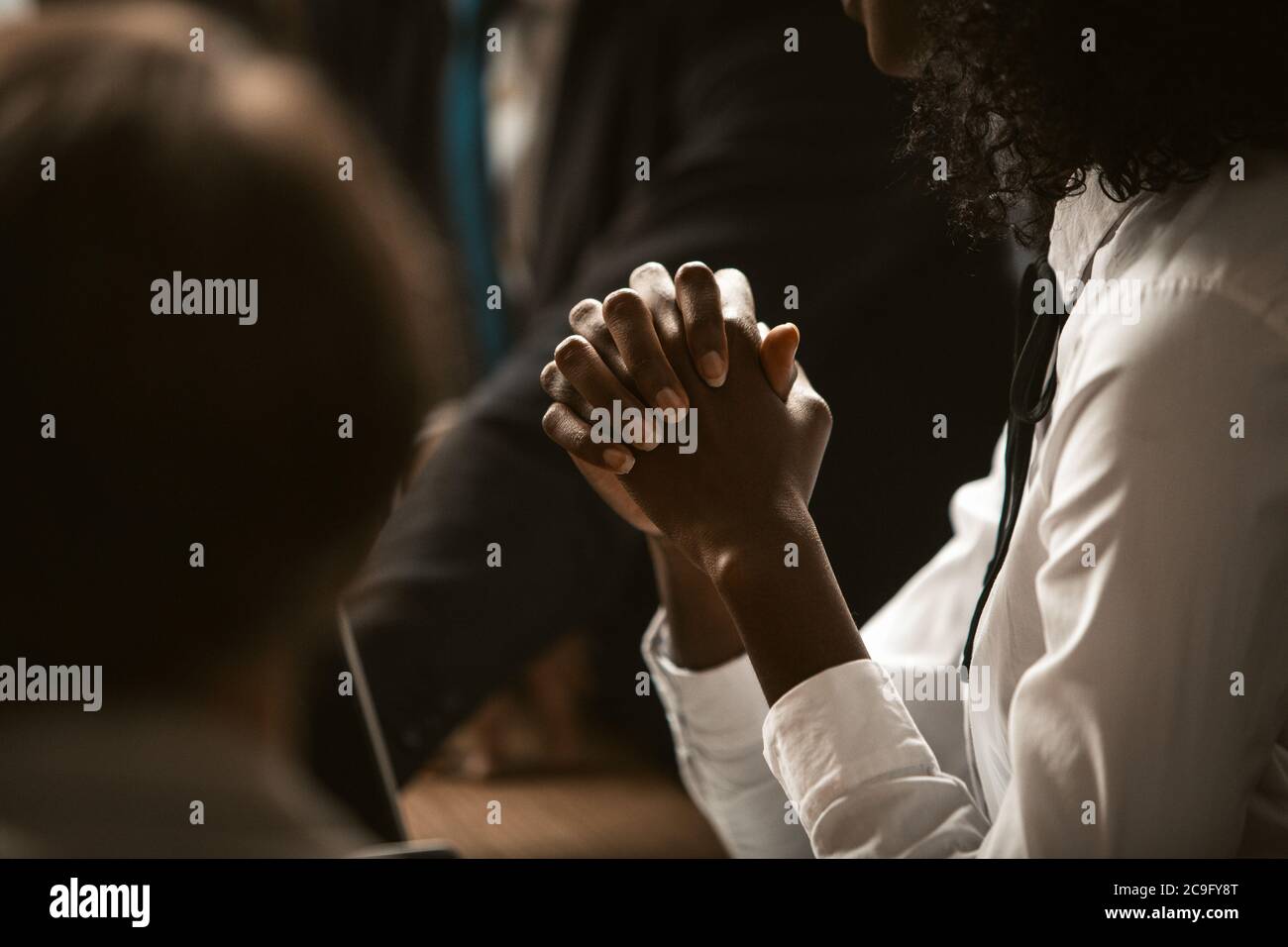 afroamerikanische Geschäftsfrau faltete die Hände, um für Geschäft zu beten. Dunkelhäutige junge Frau faltete die Hände zusammen anmutige Hände im Vordergrund. Getönt Stockfoto