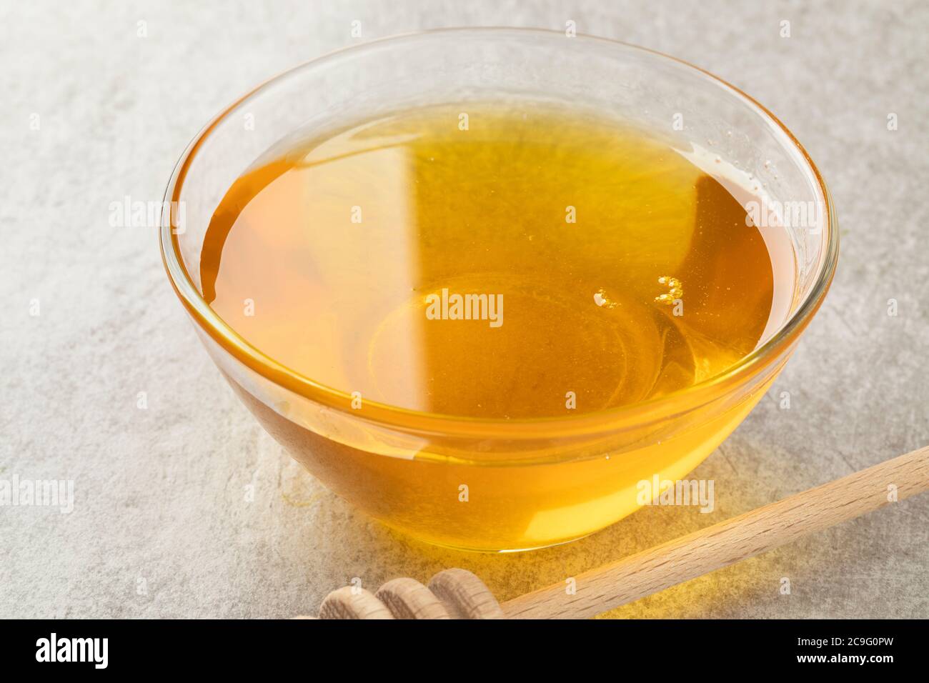 Glasschüssel mit goldenem Honig und einem hölzernen Dipper aus nächster Nähe Stockfoto