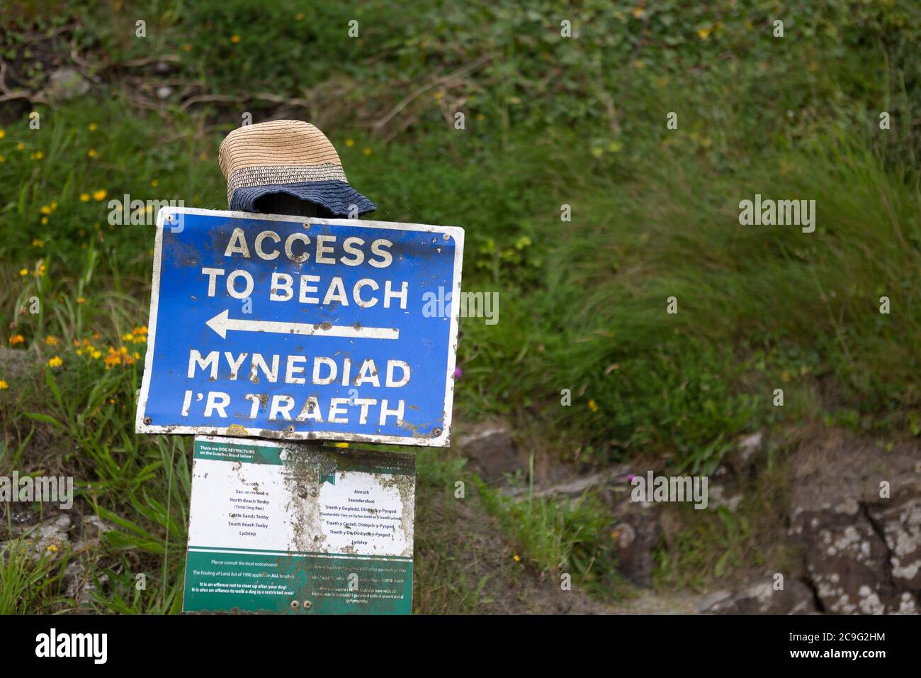 Zweisprachiges Schild in Walisisch und Englisch, das auf den Eingang zu einem Strand in Wales zeigt, mit Sonnenhut auf der Oberseite. Stockfoto