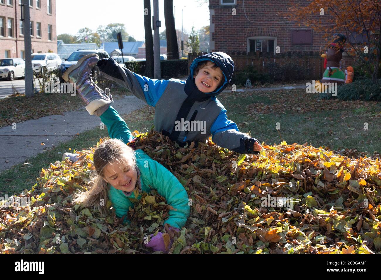 Glückliche Geschwister springen in einen Haufen von Blättern auf einem Kalter Herbsttag Stockfoto