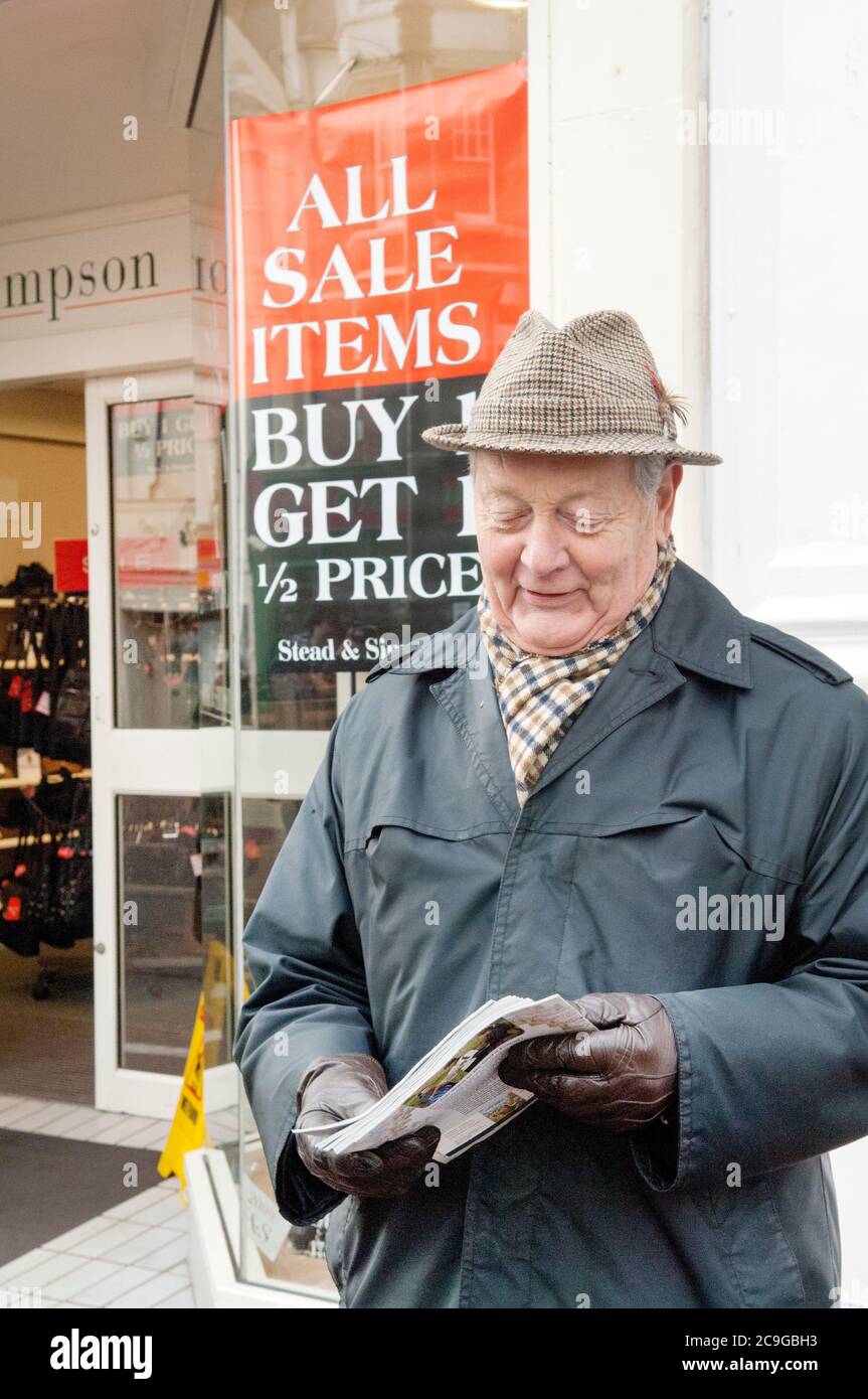 Ein älterer Herr verschenkt Cristian Literatur außerhalb eines Ladens in Bexhill on Sea, Schild im Hintergrund sagt "Alle Verkauf Artikel, kaufen 1 erhalten 1 halben Preis. Stockfoto