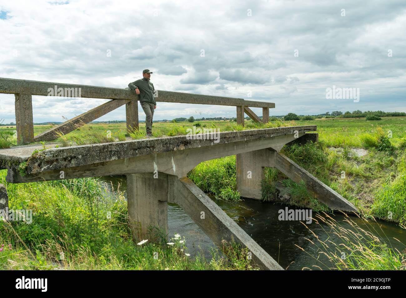 Ein Mann, der auf einer alten Brücke steht und wegschaut, Sommer Blick auf den Fluss Stockfoto