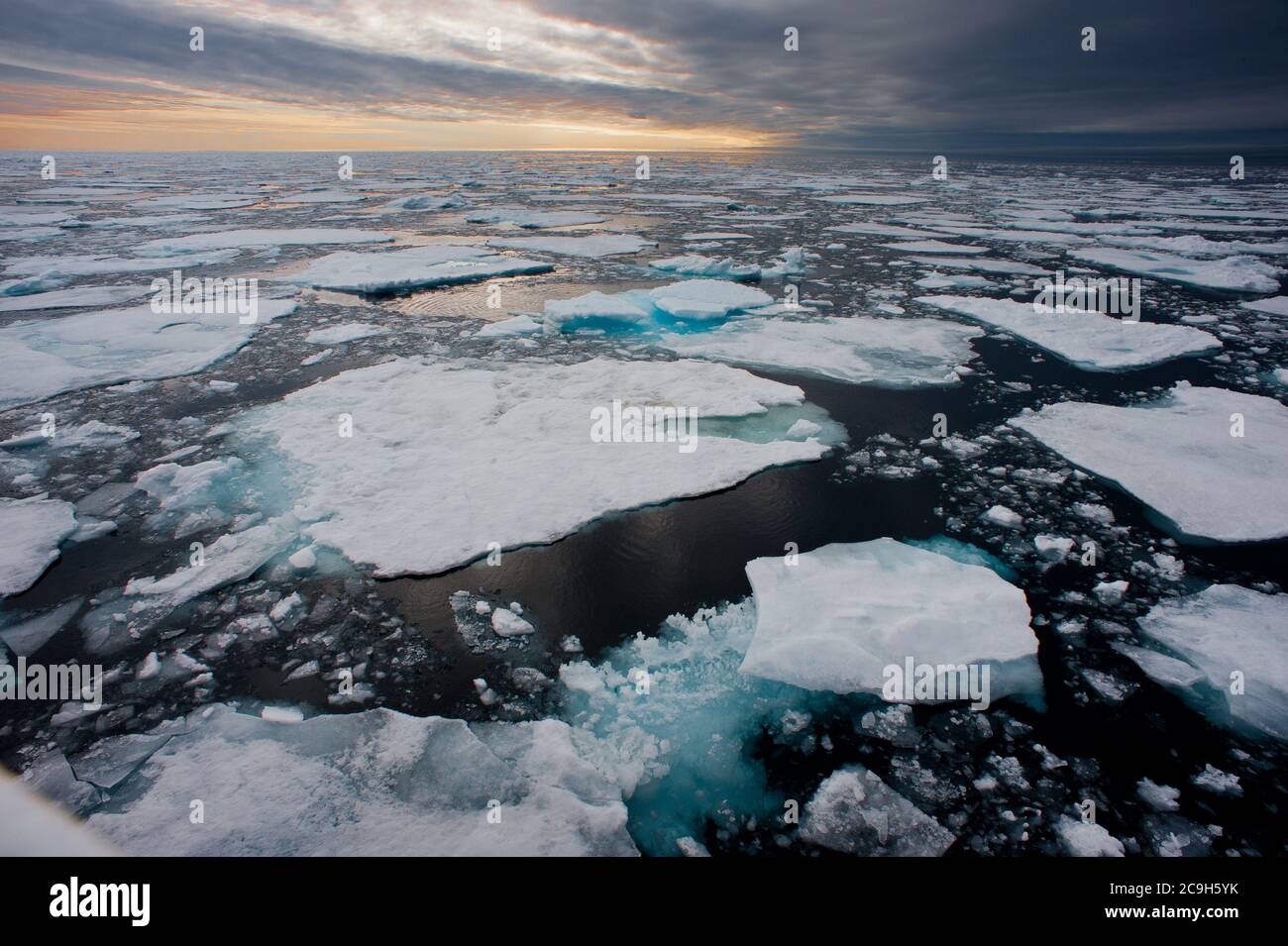 Nördliche arktische Eisschollen werden in dieser Weitwinkelansicht aufgebrochen gesehen, wobei die Sonne am Horizont untergeht.vom Schiff auf See aufgenommen. Stockfoto