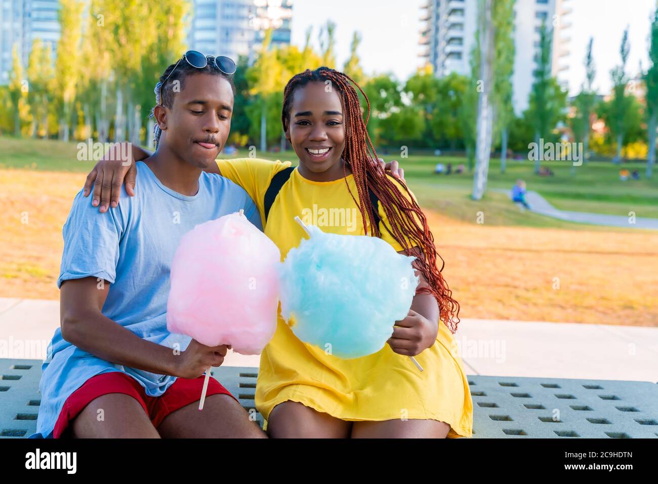 Ein glückliches schwarzes Paar, das bunte Zuckerwatte zusammen in einem Park einer großen Stadt hat. Stockfoto