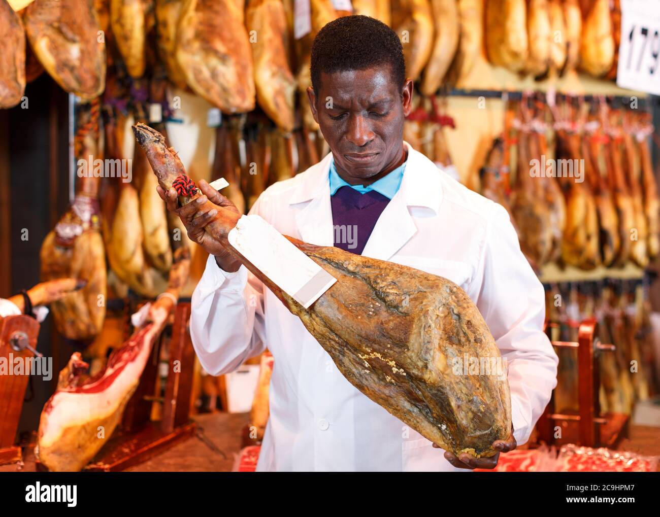 Ein erfahrener Verkäufer, der hinter der Theke in einem Delikatessengeschäft arbeitet und die Qualität von Jamon überprüft Stockfoto
