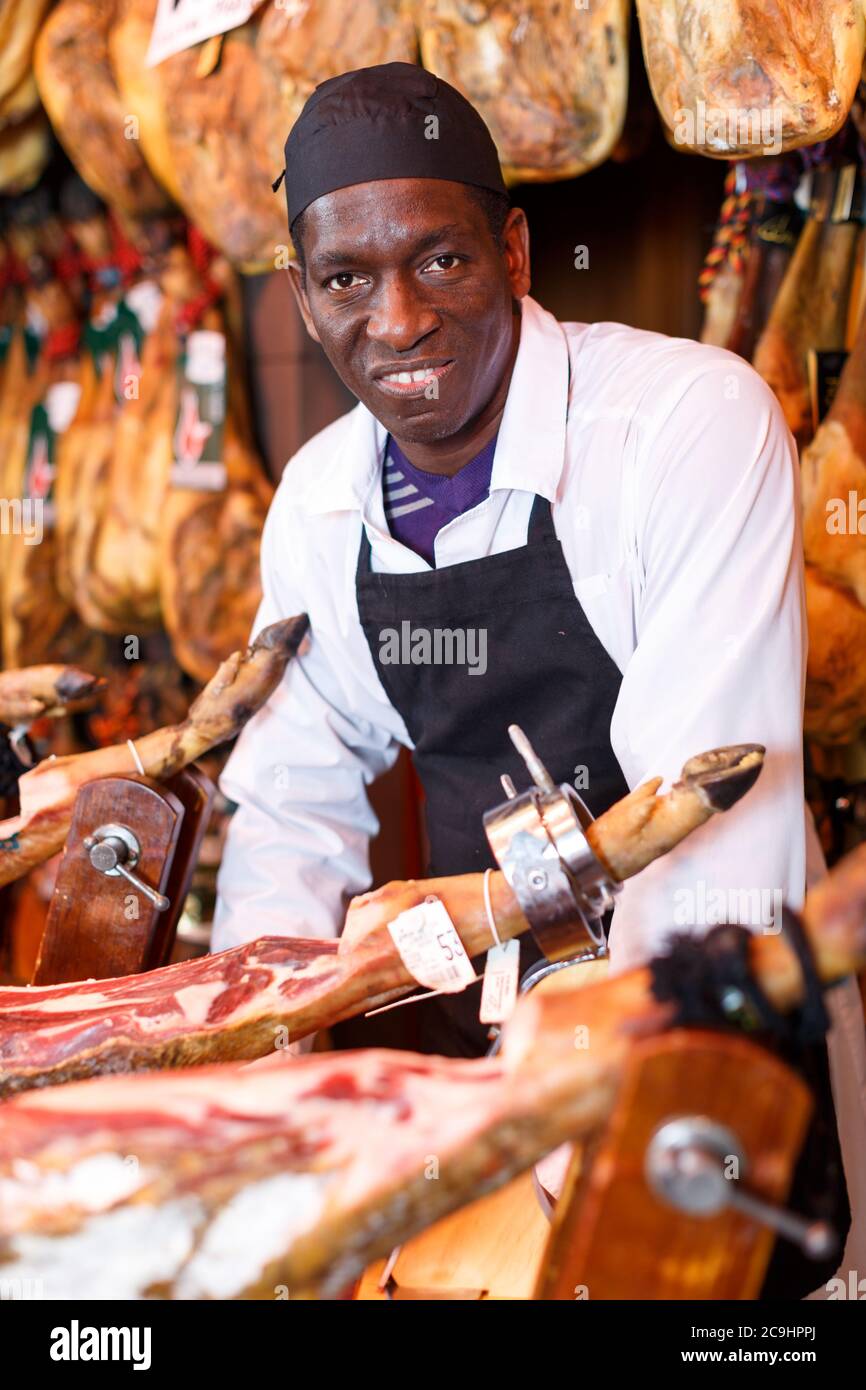 Portrait von erfahrenen Afrikaner Metzger auf dem Hintergrund der Rack mit hängenden verschiedene Jamon im Shop Stockfoto