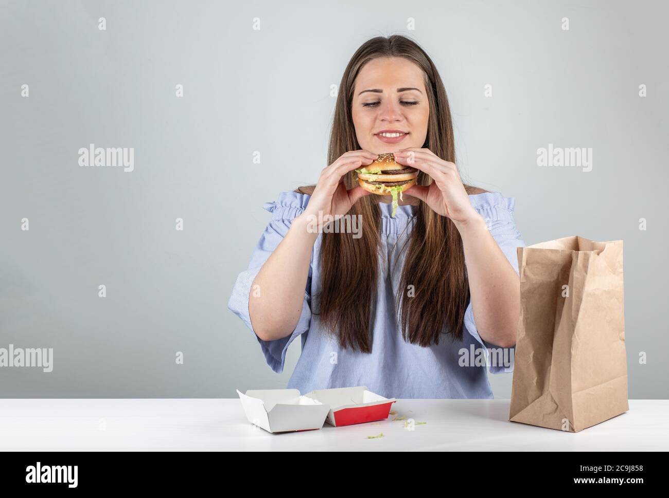 Porträt einer schönen jungen Frau essen einen Burger, isoliert auf weißem Hintergrund Stockfoto