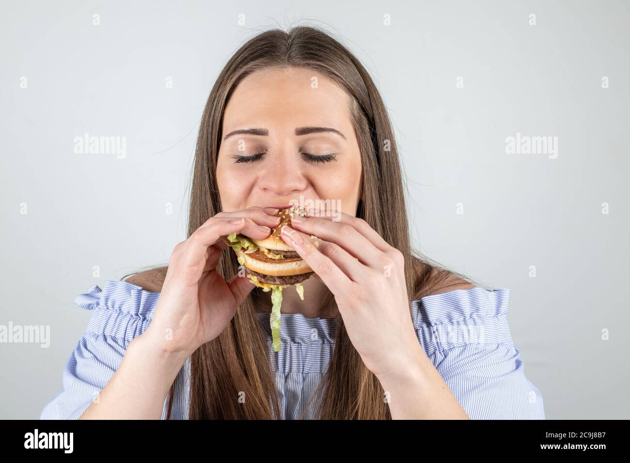 Porträt einer schönen jungen Frau essen einen Burger, isoliert auf weißem Hintergrund Stockfoto