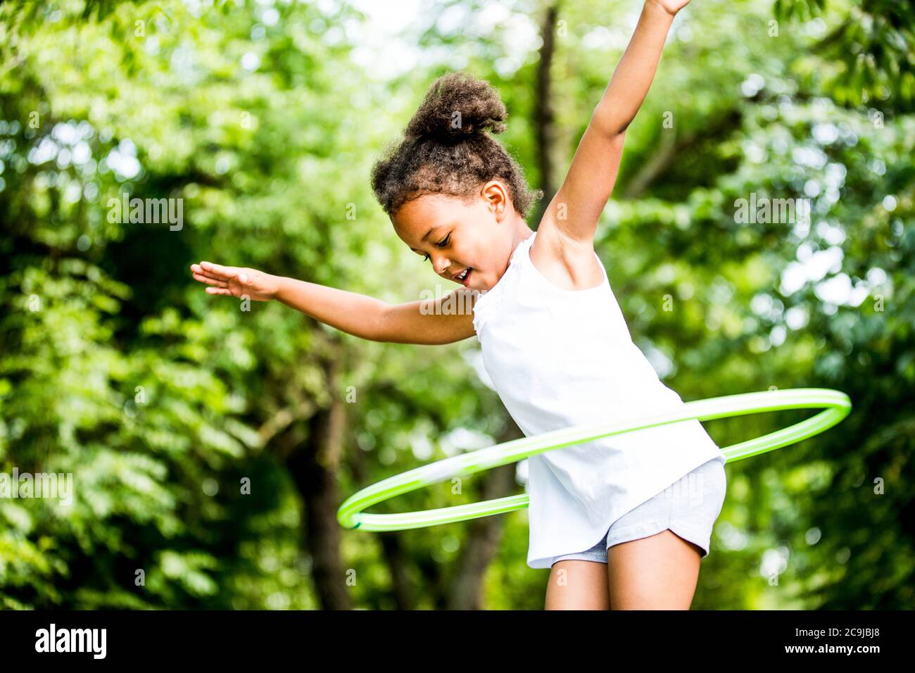 Mädchen spielt mit Hula Hoop im Park, lächelnd. Stockfoto