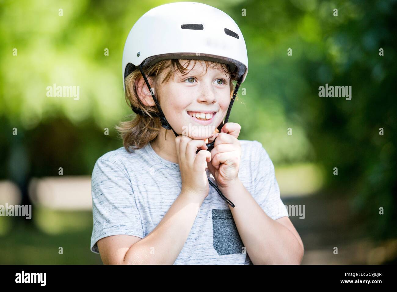Junge Befestigung Fahrradhelm im Park, lächelnd. Stockfoto