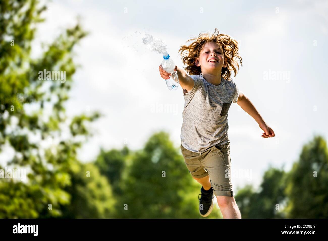Junge spritzt Wasser aus Plastikflasche, lächelnd, Porträt. Stockfoto