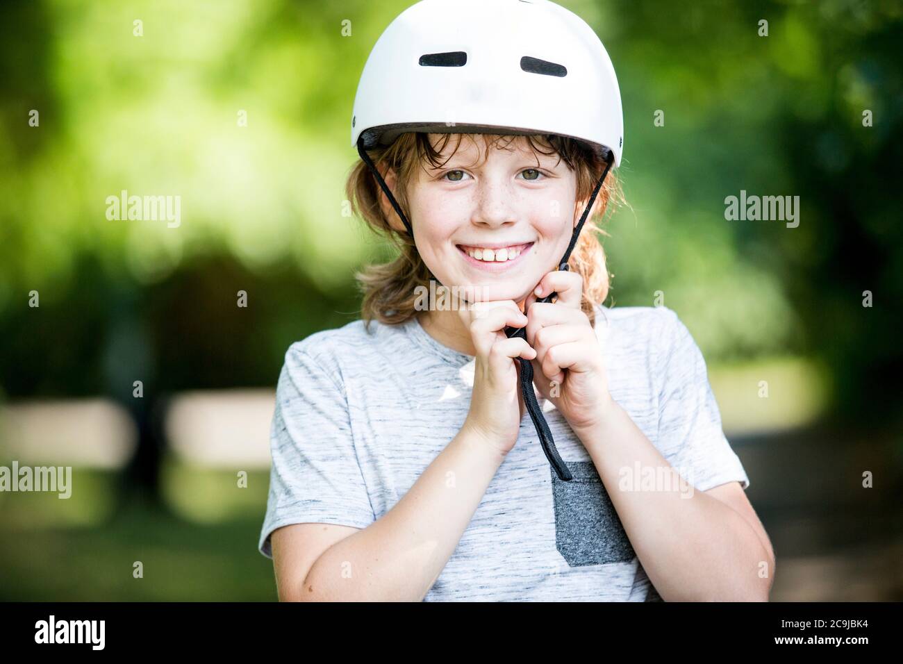 Junge Befestigung Fahrradhelm im Park, lächelnd. Stockfoto
