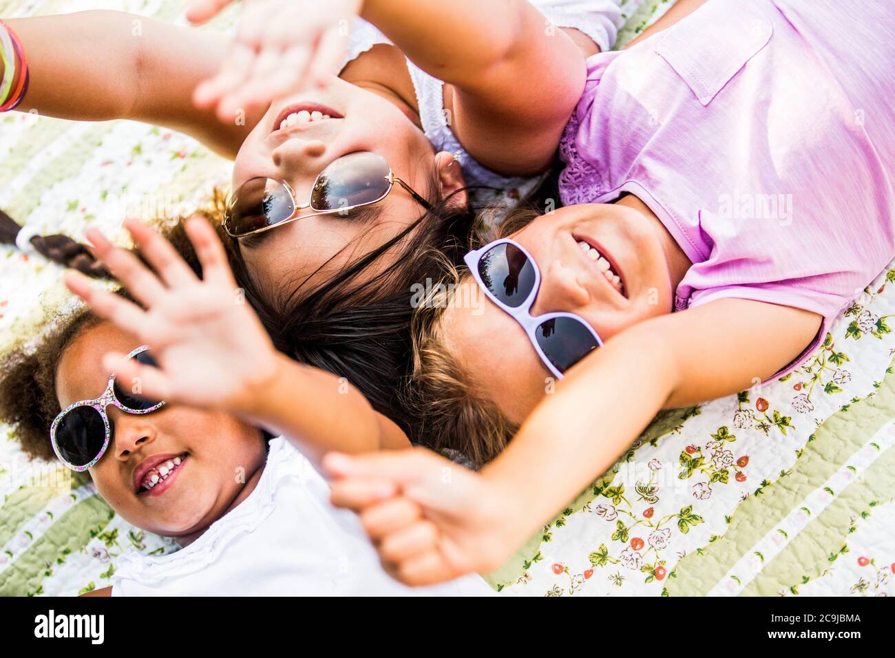 Mädchen tragen Sonnenbrillen und liegen auf einer Decke im Park. Stockfoto