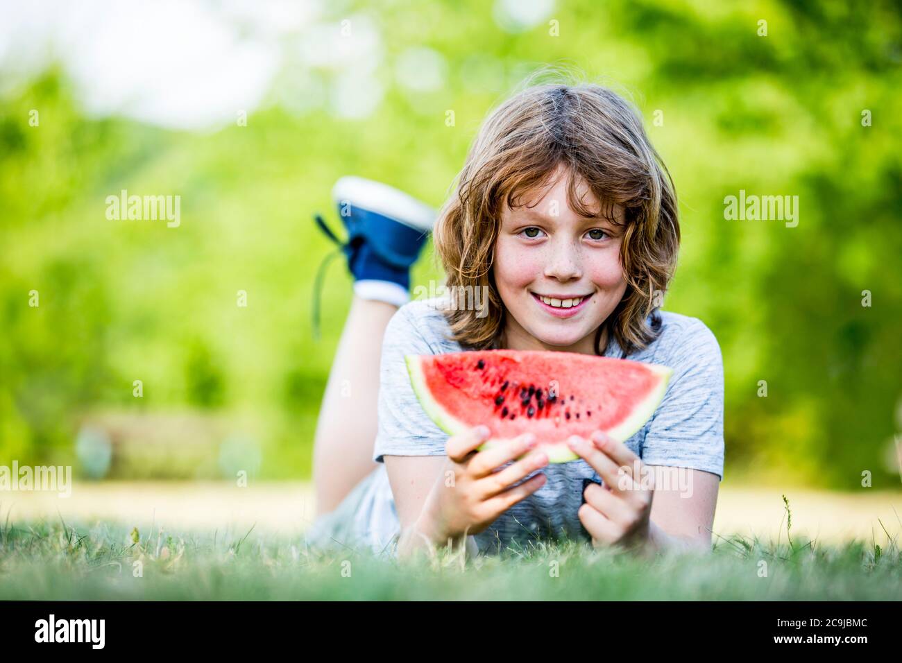 Junge hält Wassermelone, während er im Park liegt, lächelt, Porträt. Stockfoto