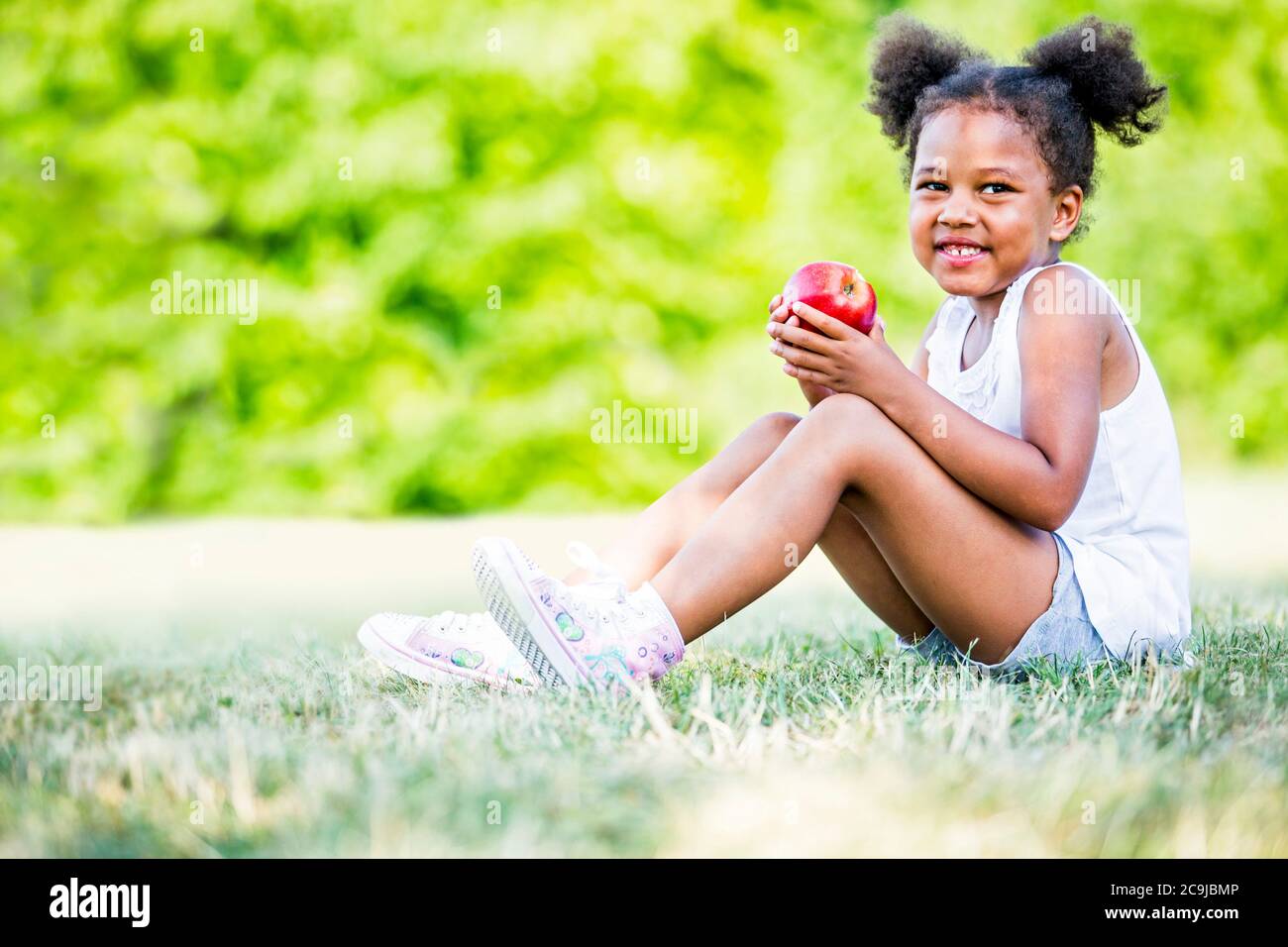 Mädchen sitzt und hält Apfel im Park. Stockfoto
