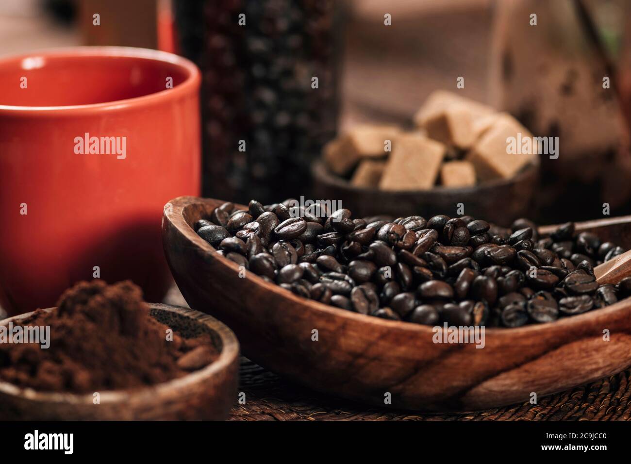 Rote Kaffeetasse, Kaffeebohnen und gemahlener Kaffee in Holzschüssel auf dem Tisch. Kaffee machen Konzept. Stockfoto