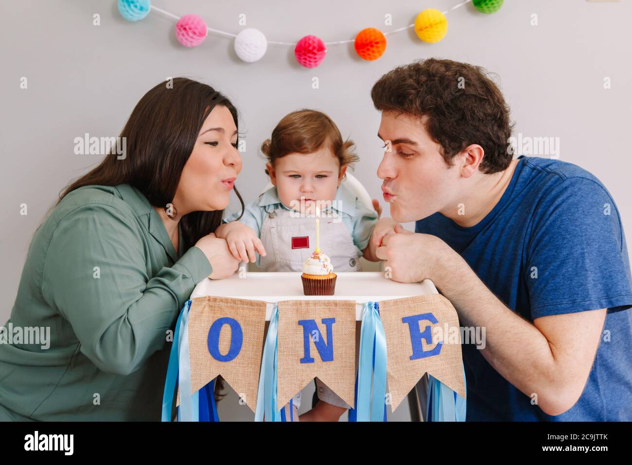 Kaukasische Familie mit Baby Jungen feiert seinen ersten Geburtstag zu Hause. Mutter Vater Papa mit Kind Kind Kleinkind weht Kerze auf Cupcake. Stockfoto