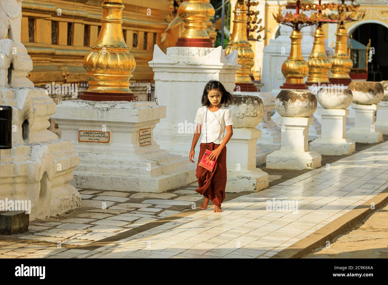Bagan/Myanmar - 4. Oktober 2019: Ein burmesisches Mädchen läuft auf einem Bürgersteig, der mit burmesischen Skulpturen in einem Tempel geschmückt ist. Stockfoto