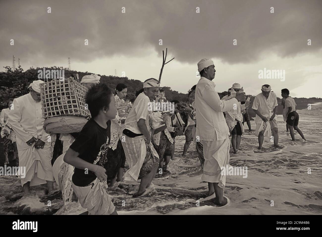 Reinigung der Geister: Ein Priester, der die Mitglieder einer balinesischen Familie zu einem Ritual am Strand von Goa Lawah in Klungkung Regency, Bali, Indonesien, führt. Stockfoto