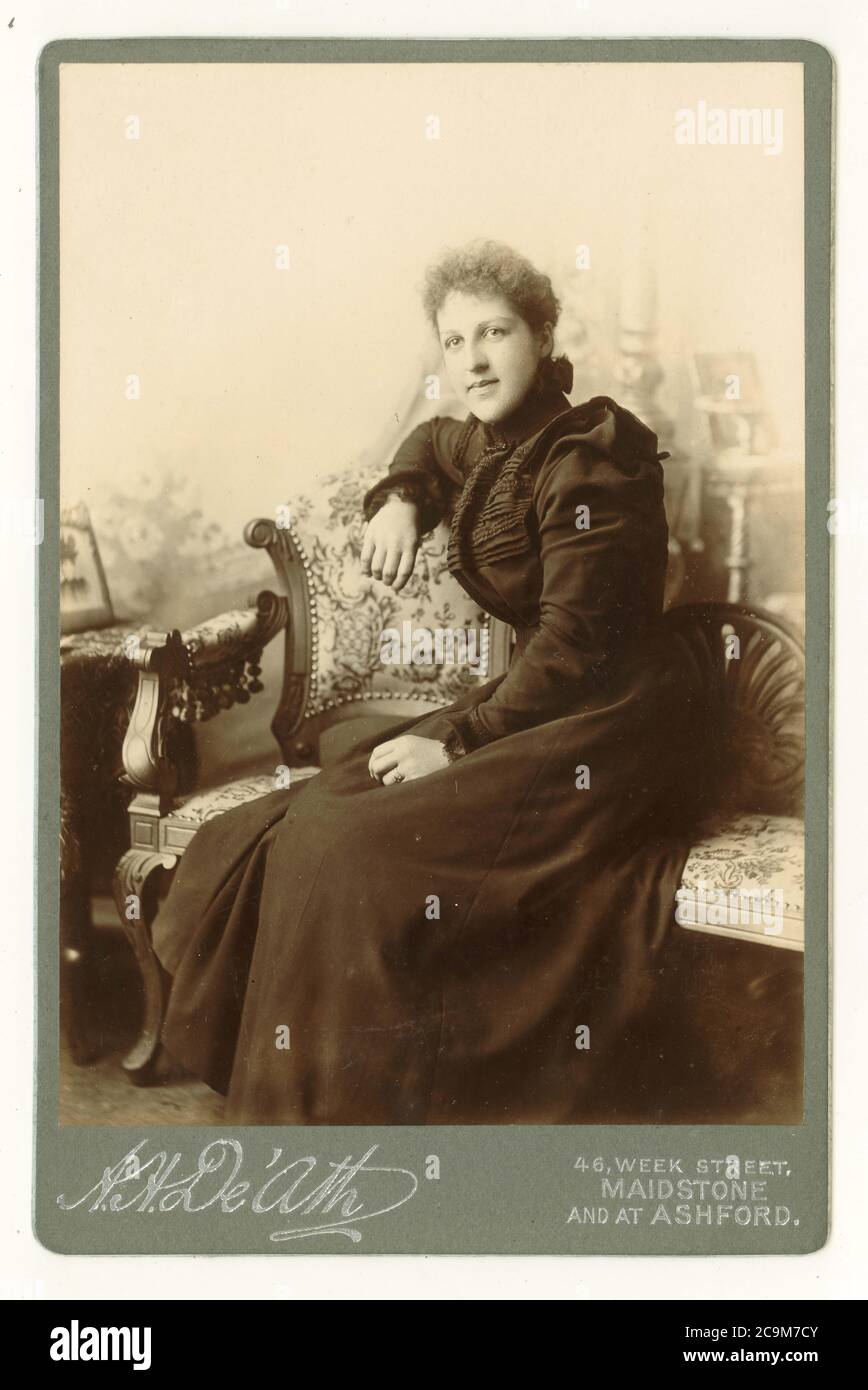 Viktorianische Schrankkarte posierte Atelierporträt mit Requisiten, einer hübschen jungen viktorianischen Frau in modischem Kleid mit Schulter mit Hammelärmeln, datiert vom Juli 1899, Maidstone, Kent, England. GROSSBRITANNIEN Stockfoto