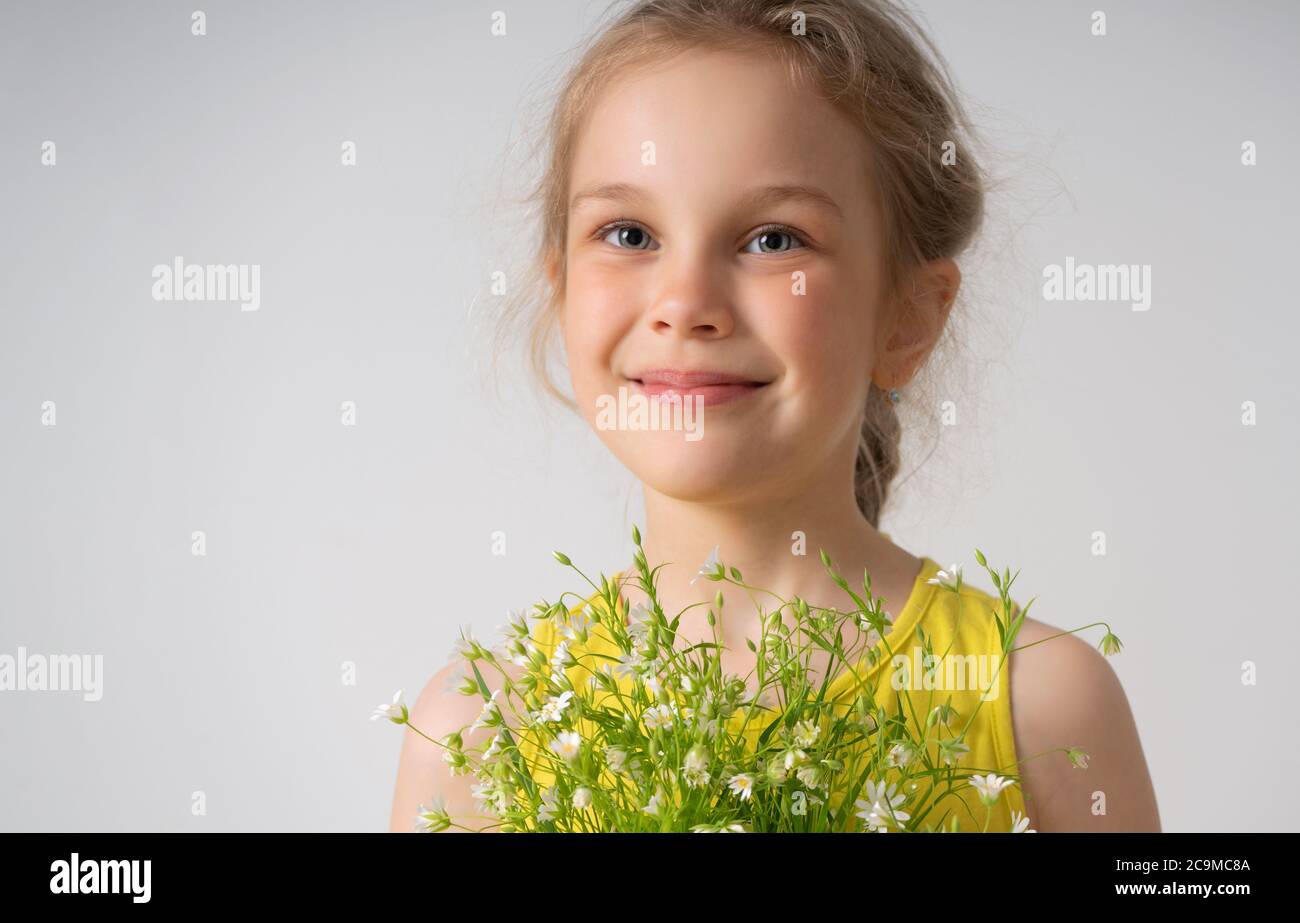 Nahaufnahme Porträt eines fröhlichen lächelnden kleinen Mädchen in gelb gekleidet hält Bündel von Feld Blumen in den Händen. Studio Shot isoliert auf weiß Stockfoto