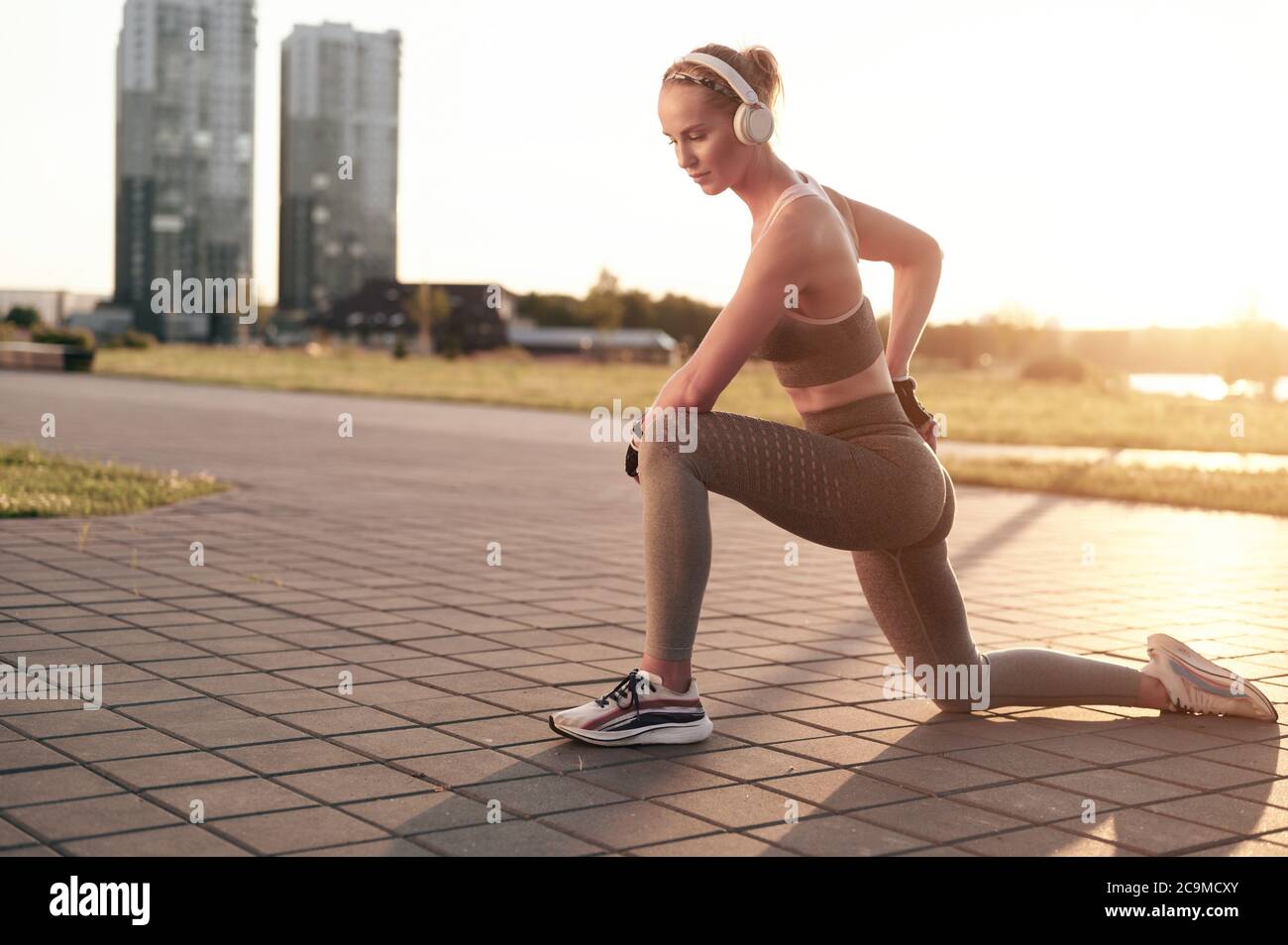 Junge sportliche Frau in Kopfhörer tun Stretching im Park in der Stadt Blick, starke Beine und abs, muskulöse Arme, Fitness trägt Mädchen Stockfoto