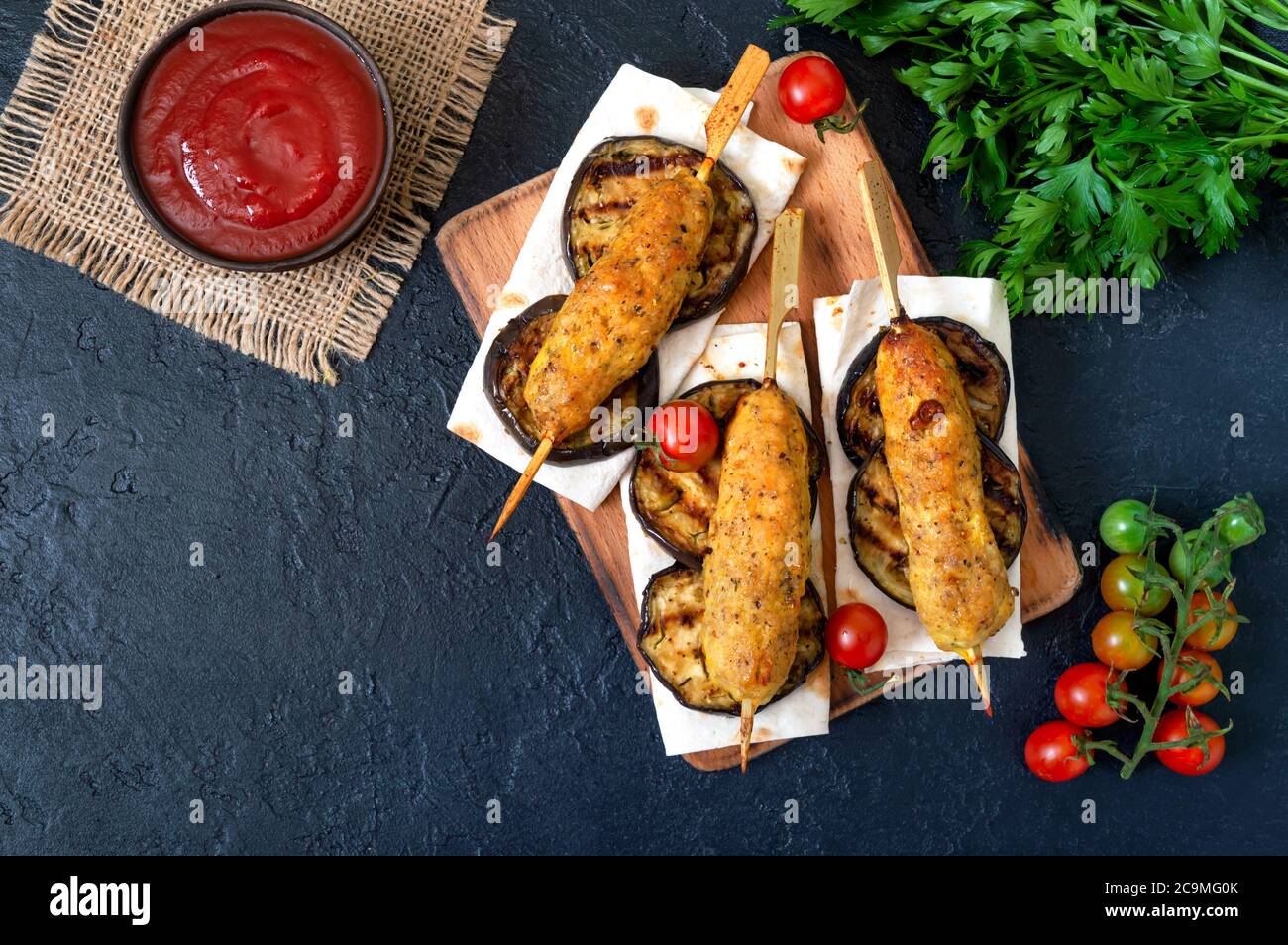 Lula Kebab mit gegrillter Aubergine auf Pita-Brot. Hähnchenkebab auf einem Spieß mit Gemüse auf dem schwarzen. Stockfoto