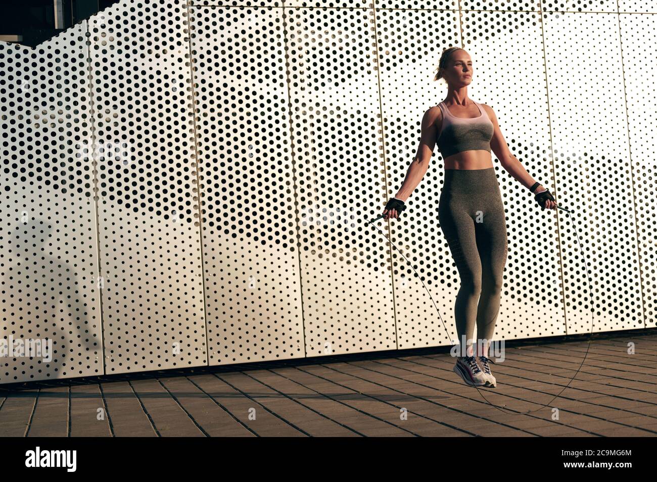 Starke sportliche Frau trägt Sportbekleidung tun körperliche Übungen mit Springseil Abend im Freien. Stockfoto