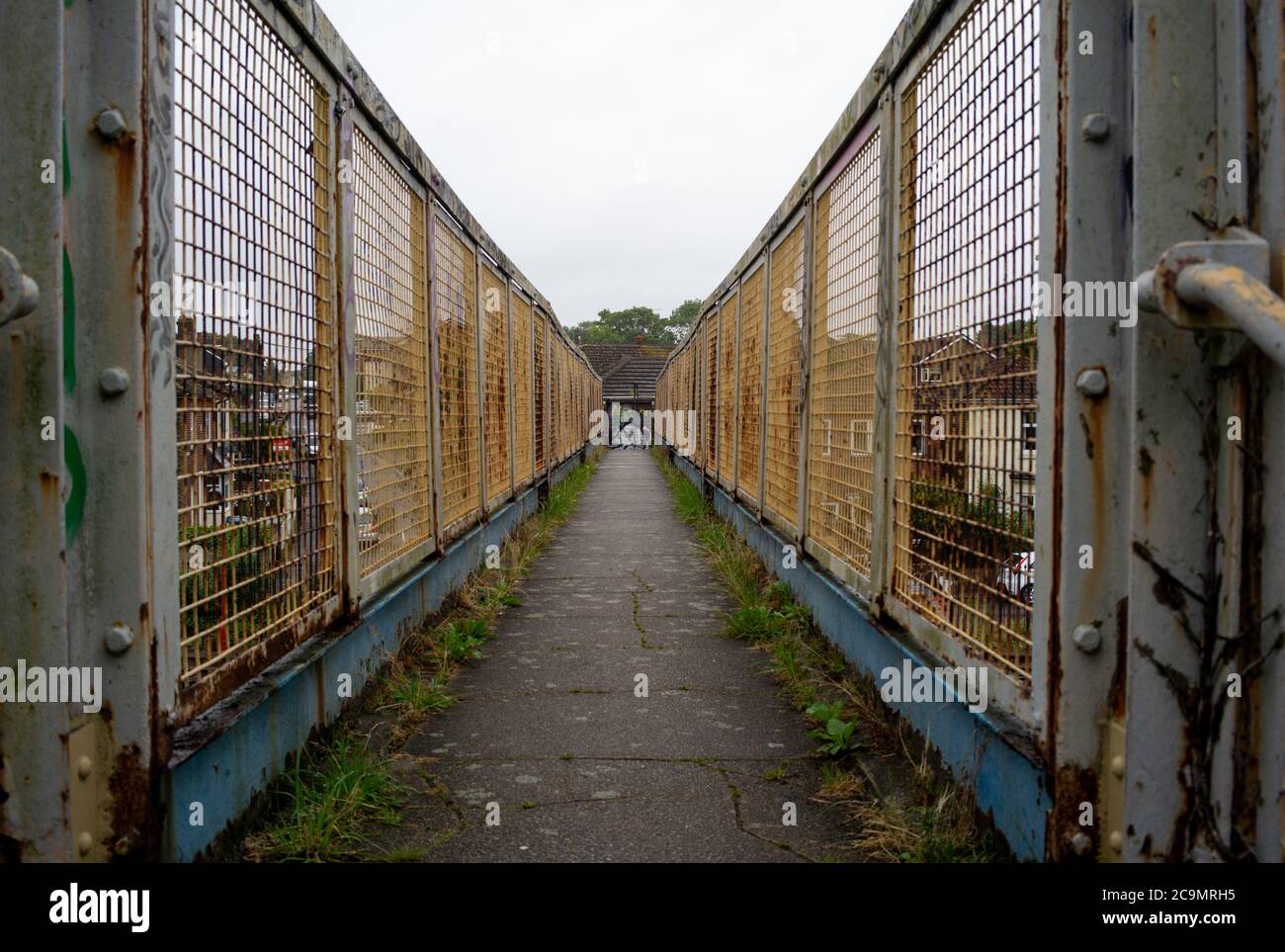 Ein allgemeiner Blick auf eine schmale Eisenbahnfußbrücke, die verwittert ist, rostig mit einigen Graffiti, die Perspektive und führende Linien zeigen. Stockfoto