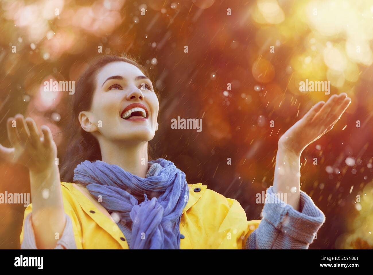 Glückliche schöne junge Frau unter der Herbstdusche. Mädchen trägt gelben Regenmantel und genießen Niederschläge. Stockfoto