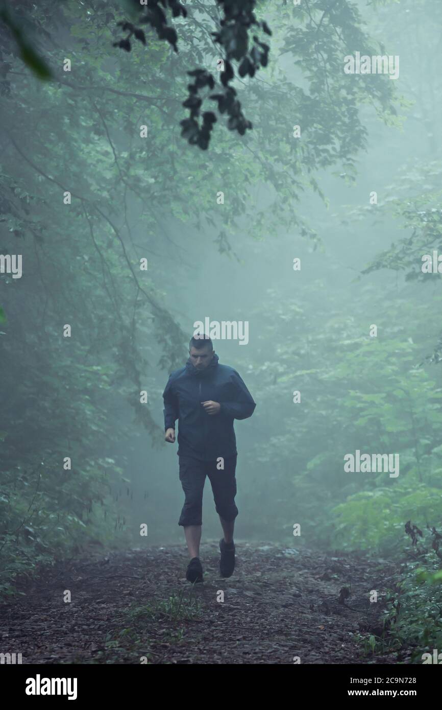 Männlicher Läufer mittleren Alters, läuft durch nebligen Waldweg, früh am Morgen. Stockfoto