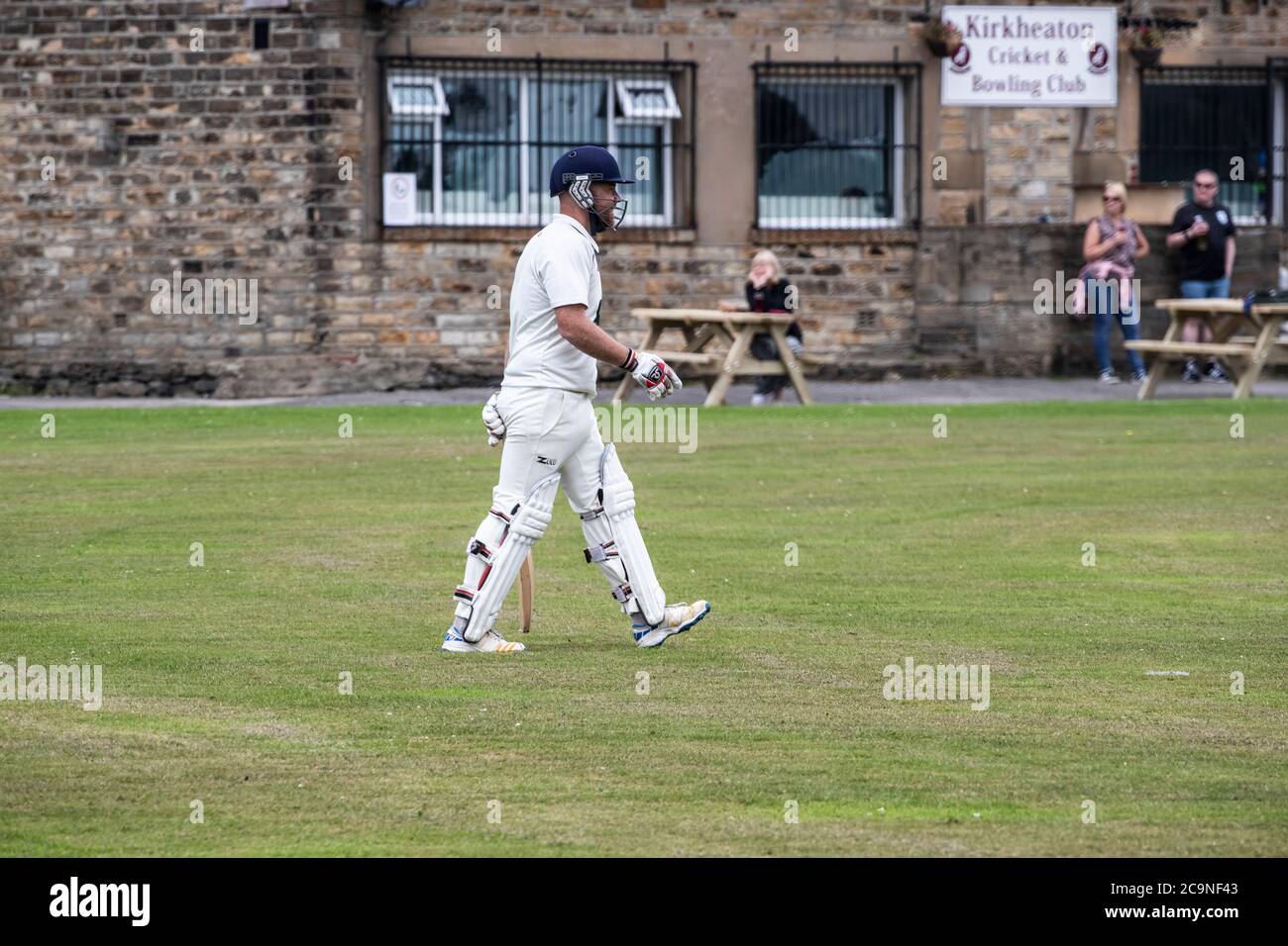 New Batsman in einem Dorf Cricket-Spiel in West Yorkshire nehmen das Feld in Pads, Handschuhe und Helm mit einem Cricket-Schläger an einem Samstagnachmittag Stockfoto