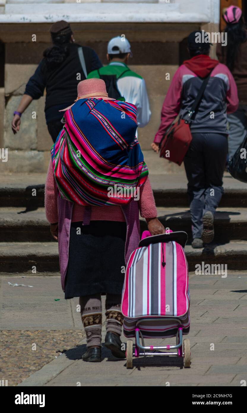 COPACABANA, BOLIVIEN - 24. JULI 2016: Eine bolivianische Frau trägt einen traditionellen Stofftyp namens 'aguayo' und einen modernen Einkaufswagen für Einkaufstüten in Copacaba Stockfoto