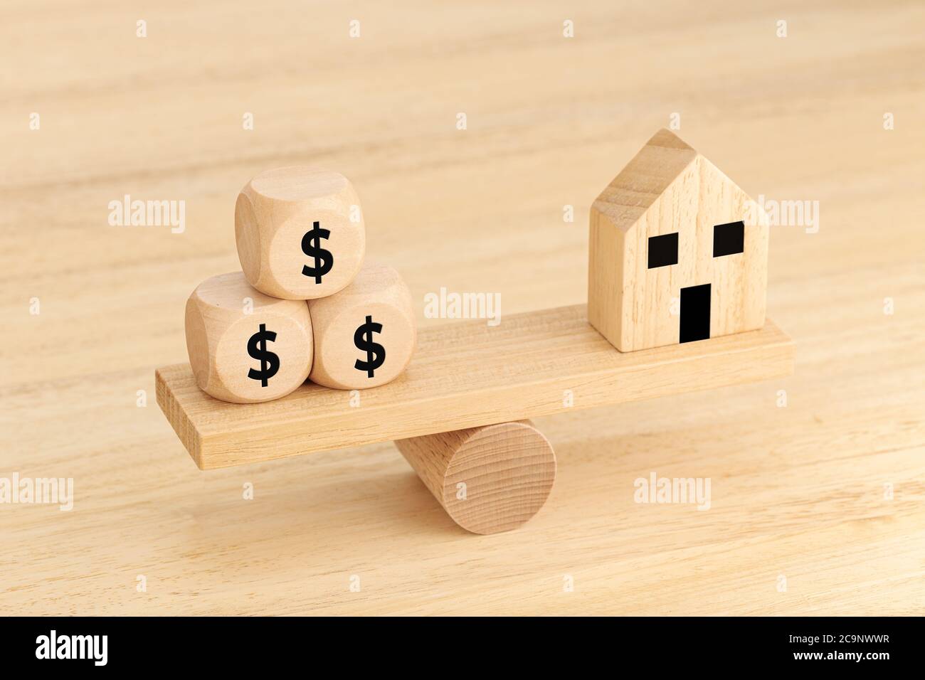 Hauskauf-Konzept. Spielzeughaus aus Holz und Würfel aus Holz mit Dollarzeichen auf der Wippe Stockfoto