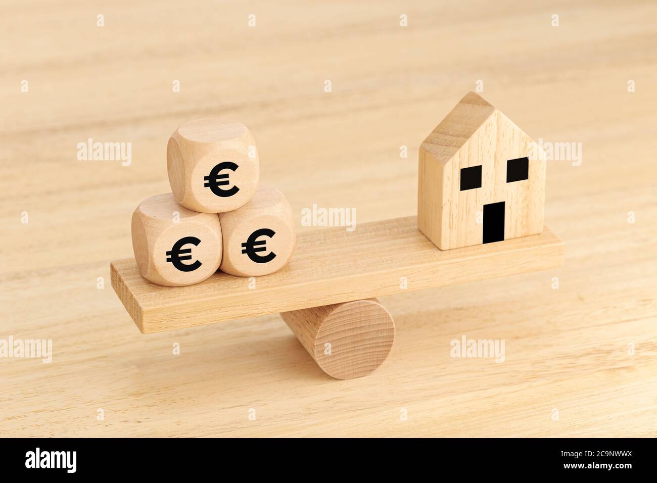 Hauskauf-Konzept. Holzspielzeughaus und Holzwürfel mit Euro-Symboltext auf Wippe Stockfoto