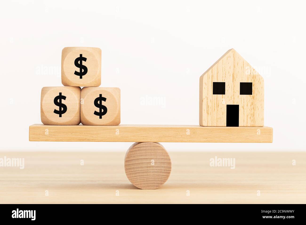 Hauskauf-Konzept. Spielzeughaus aus Holz und Würfel aus Holz mit Dollarzeichen auf der Wippe Stockfoto