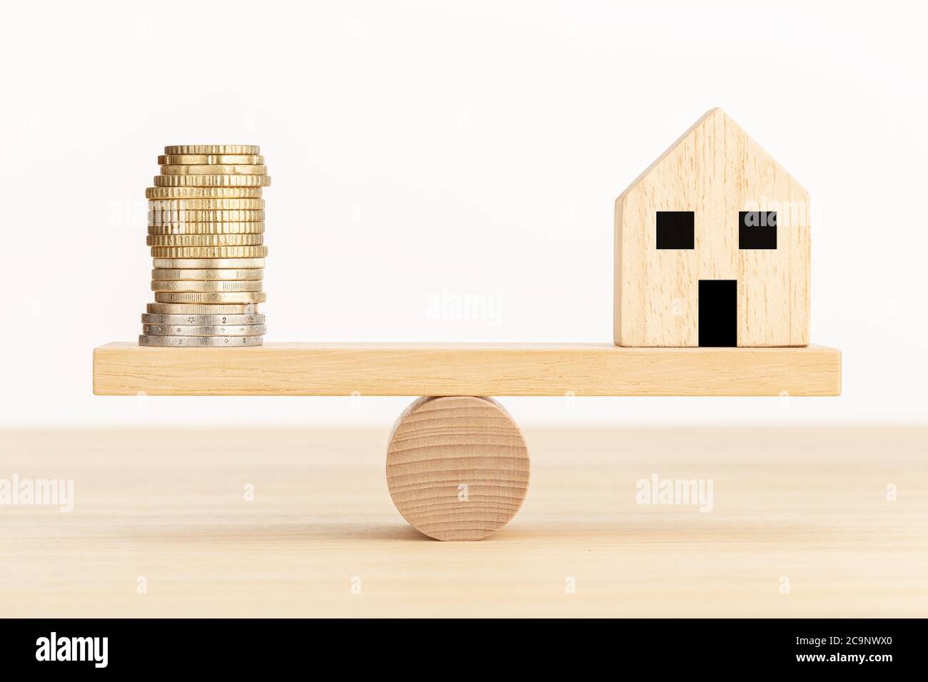 Hauskauf-Konzept. Holzspielzeughaus und Münze auf Wippe Stockfoto