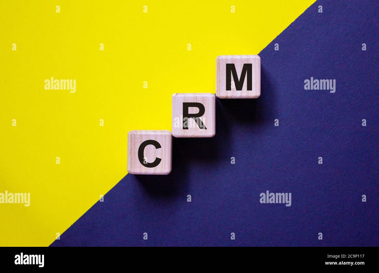Holzwürfel mit Wort 'CRM' Stapeln als Treppenstufe auf Papier blau und gelb Hintergrund, kopieren Raum. Geschäftskonzept. Stockfoto