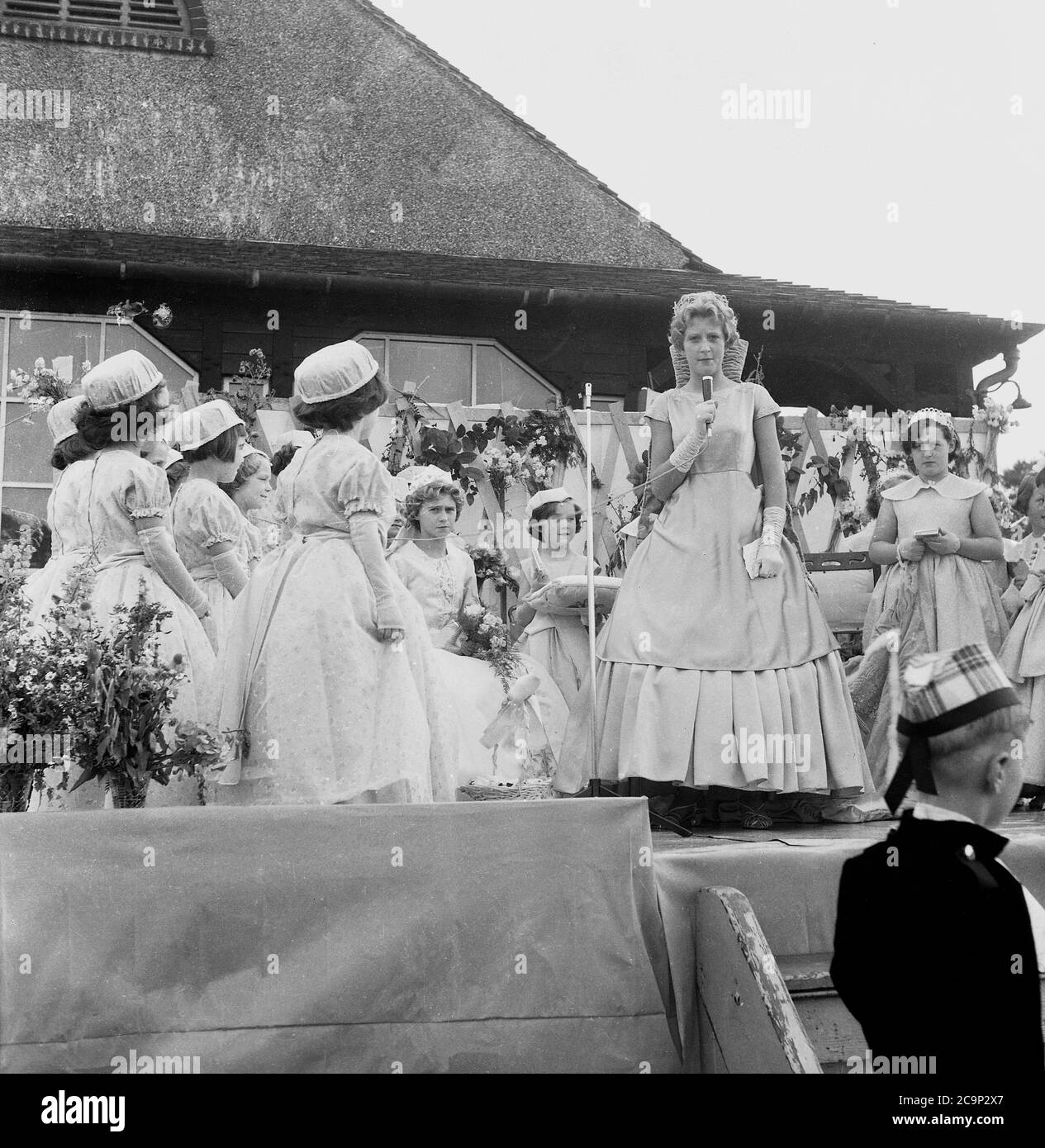 1950er Jahre, historisch, auf einer Plattform vor einem hölzernen Sportpavillon in Farnworth, Lancashire, der neu gekrönten "Rosenkönigin" der Stadt, eine Rede zu halten. In einem Seidenkleid und mit einer Tiara wird das Mädchen die traditionelle Prozession oder Parade führen, die als "Walking Day" bekannt ist, Feiern, die in dieser Zeit im Nordwesten Englands, Großbritannien, üblich waren. Ein jährliches Ereignis, einige stammen aus den 1830er Jahren, wo sie Kirchenparaden waren und viele werden noch heute abgehalten. Stockfoto