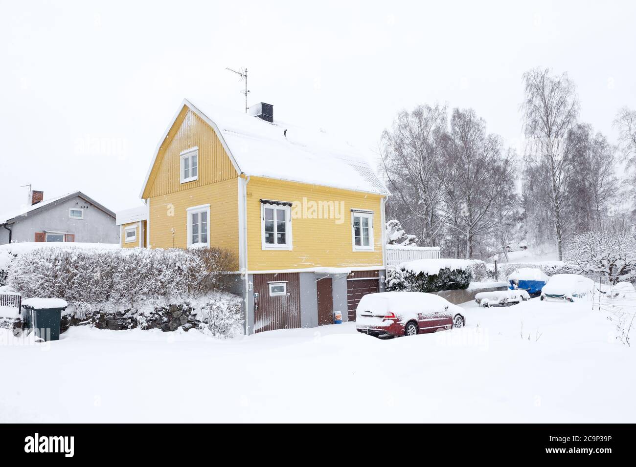Gelbes schwedisches zweistöckiges Einfamilienhaus mit einem kaputten Dach, das in den späten 1940er Jahren während des Schneefalls in der Wintersaison gebaut wurde. Stockfoto