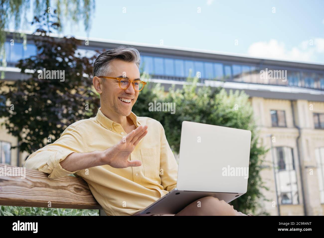 Schöner reifer Geschäftsmann mit Laptop, Arbeitsprojekt, beobachten Schulungen, sitzen auf Bank. Lächelnder Mann mit Videokonferenz Stockfoto